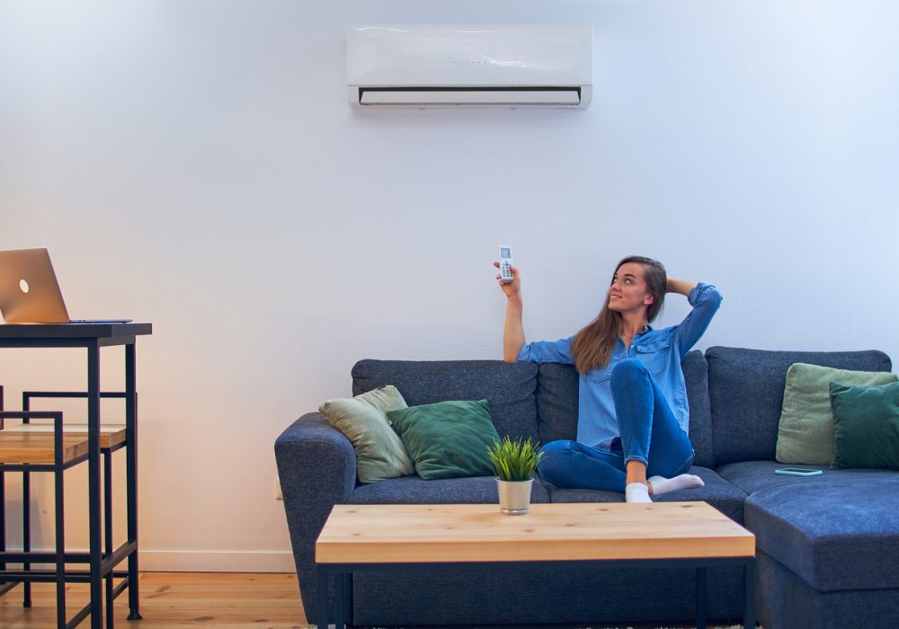young-happy-woman-sitting-couch-air-conditioner-adjusting-comfort-temperature-with-remote-control-modern-home_Easy-Resize.com